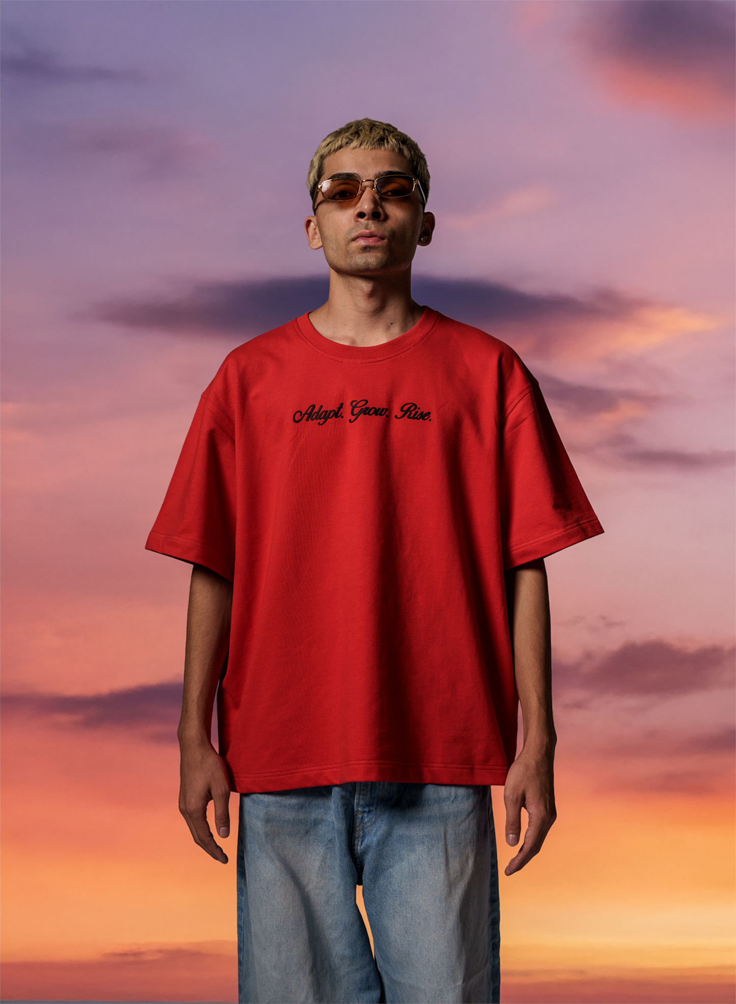 Man wearing a red t-shirt with text against a colorful sky